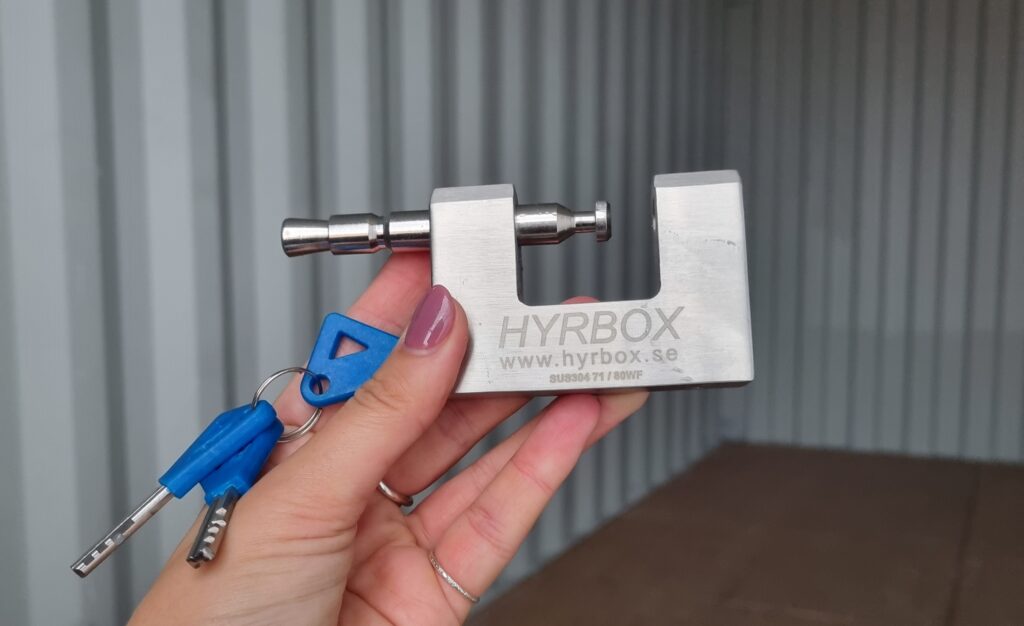 HyrBox hänglås med två nycklar, hållet framför en öppen förrådscontainer